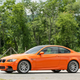Side view of an orange BMW M3 parked in front of trees.